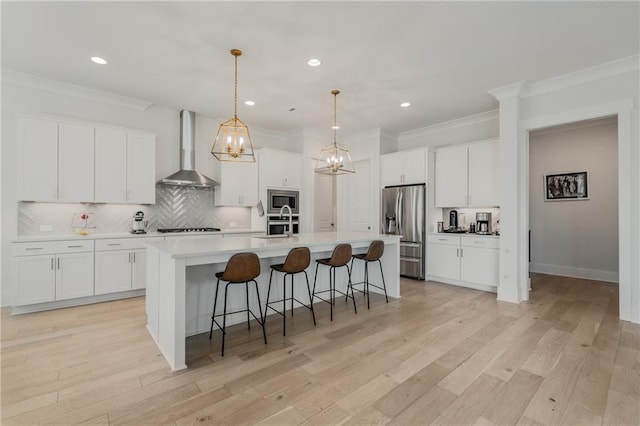 kitchen featuring a kitchen bar, stainless steel appliances, a center island with sink, light wood-type flooring, and wall chimney exhaust hood