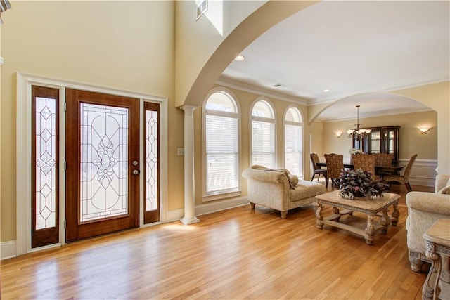 foyer entrance with arched walkways, crown molding, light wood-style floors, and ornate columns