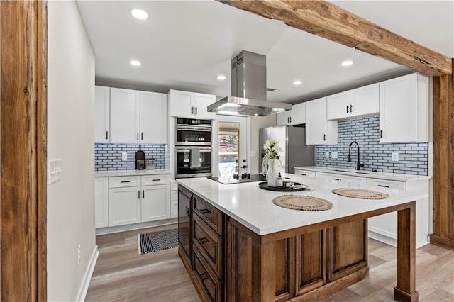 kitchen featuring light countertops, appliances with stainless steel finishes, island exhaust hood, white cabinetry, and a sink