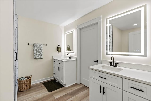 bathroom with wood finished floors, two vanities, baseboards, and a sink