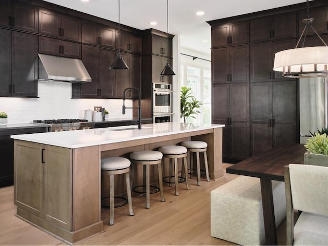 kitchen featuring sink, decorative light fixtures, light hardwood / wood-style flooring, an island with sink, and stainless steel appliances