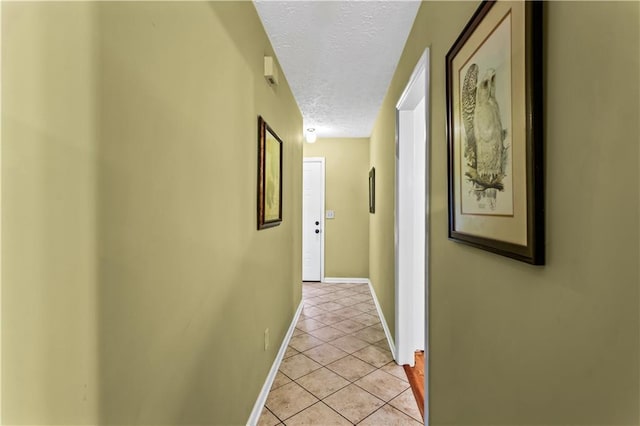 corridor featuring a textured ceiling, light tile patterned floors, and baseboards
