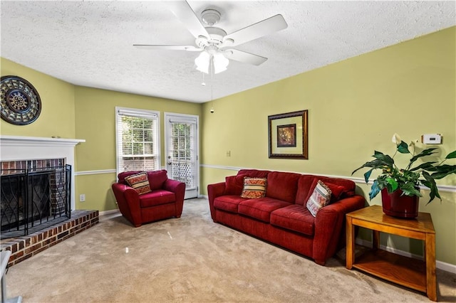 living area featuring a textured ceiling, carpet floors, a ceiling fan, baseboards, and a brick fireplace