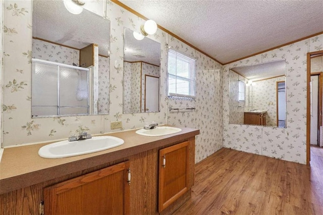 bathroom with a sink, a textured ceiling, a stall shower, and wallpapered walls