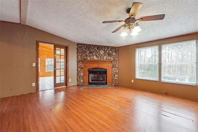 unfurnished living room featuring a stone fireplace, lofted ceiling, light wood-style flooring, and a textured ceiling