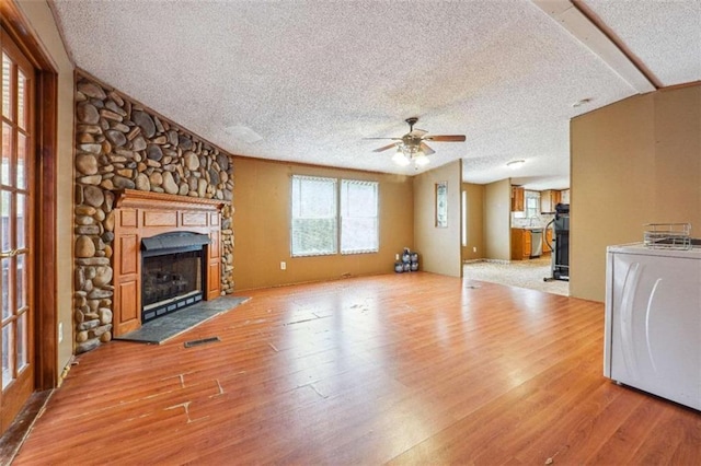 unfurnished living room featuring a textured ceiling, wood finished floors, a stone fireplace, washer / dryer, and ceiling fan