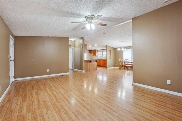 unfurnished living room featuring light wood-type flooring, lofted ceiling, ceiling fan with notable chandelier, a textured ceiling, and baseboards