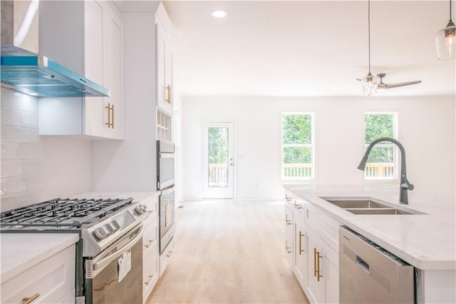 kitchen with stainless steel appliances, wall chimney range hood, white cabinets, and sink