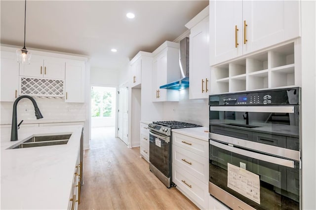 kitchen with wall chimney exhaust hood, decorative light fixtures, white cabinets, appliances with stainless steel finishes, and sink