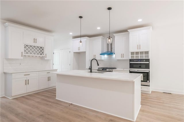 kitchen with a kitchen island with sink, wall chimney exhaust hood, tasteful backsplash, and white cabinetry