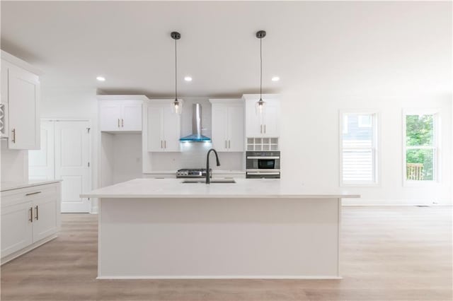 kitchen with sink, pendant lighting, an island with sink, and wall chimney range hood