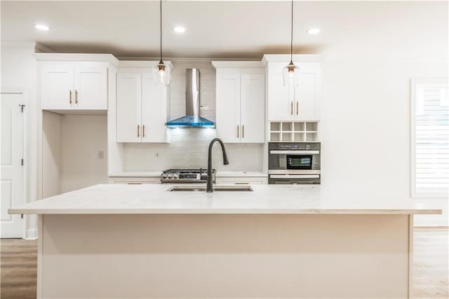 kitchen with hanging light fixtures, an island with sink, light stone countertops, wall chimney exhaust hood, and sink