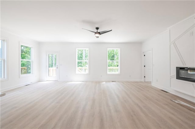 unfurnished living room featuring heating unit, ceiling fan, a wealth of natural light, and light wood-type flooring