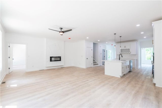 kitchen with hanging light fixtures, an island with sink, white cabinetry, ceiling fan, and sink