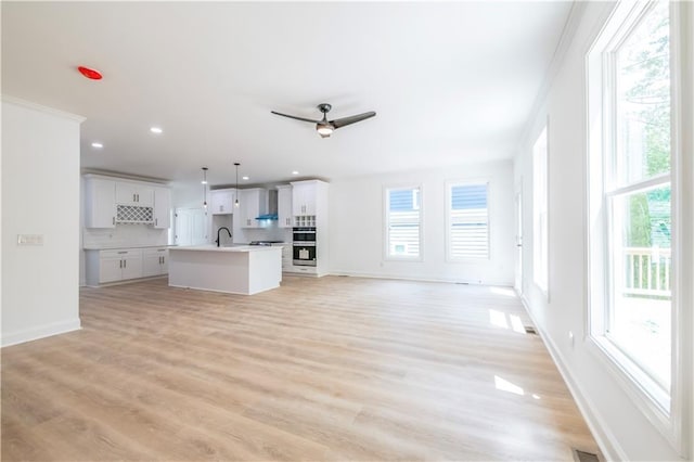 unfurnished living room with sink, ornamental molding, and plenty of natural light