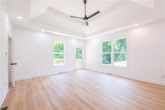 empty room featuring light wood-type flooring, ceiling fan, and a tray ceiling