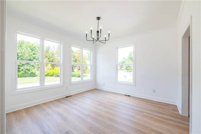 unfurnished dining area featuring an inviting chandelier, ornamental molding, a wealth of natural light, and light hardwood / wood-style flooring