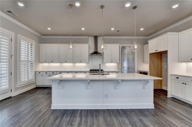 kitchen featuring crown molding, visible vents, white cabinets, a sink, and wall chimney range hood