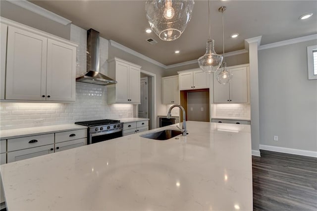 kitchen featuring visible vents, gas range, ornamental molding, wall chimney range hood, and a sink