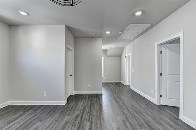 unfurnished room with attic access, baseboards, visible vents, and dark wood-type flooring