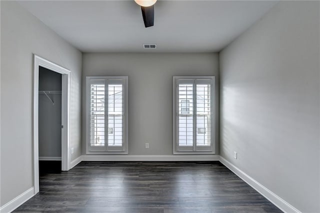 unfurnished bedroom with a closet, dark wood finished floors, visible vents, and baseboards