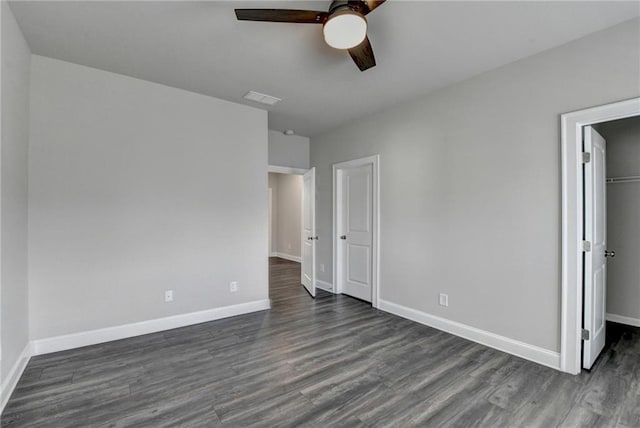 unfurnished bedroom with a closet, visible vents, a spacious closet, dark wood-type flooring, and baseboards