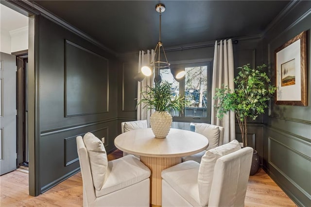 dining area featuring light wood-style flooring, a chandelier, a decorative wall, and crown molding