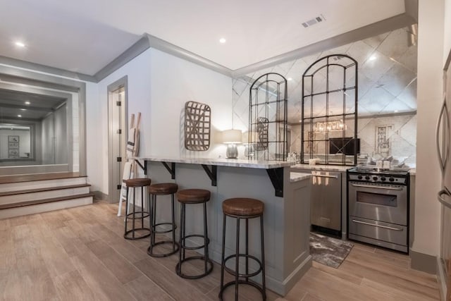 bar with light stone countertops, gray cabinetry, stainless steel appliances, crown molding, and a notable chandelier