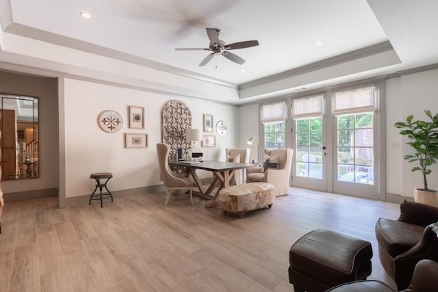 living area featuring ceiling fan, light hardwood / wood-style floors, and a tray ceiling