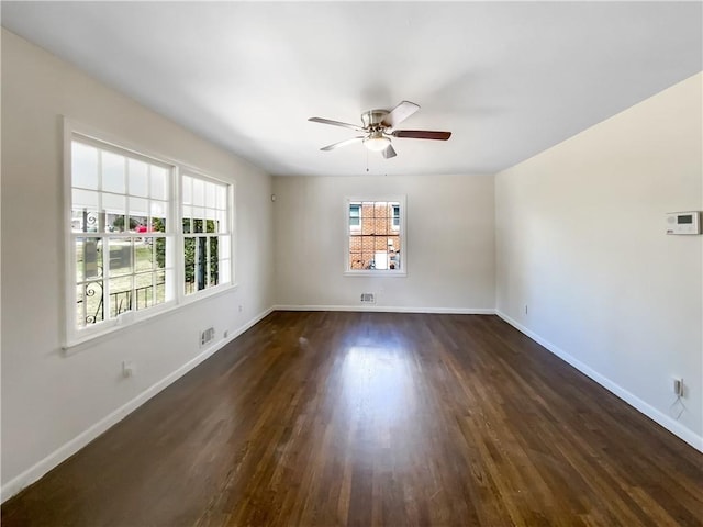 empty room with dark wood-style flooring, a ceiling fan, and baseboards