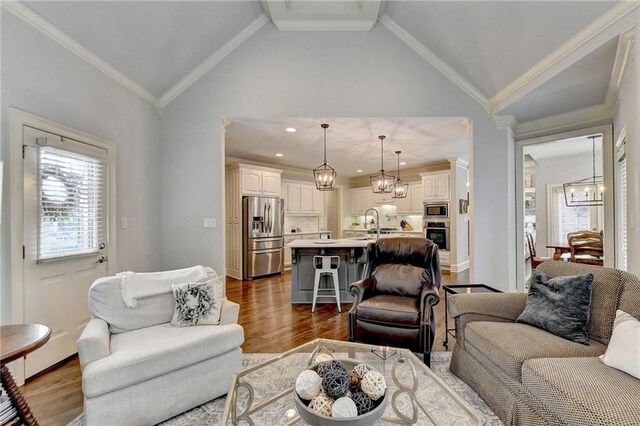 living room featuring sink, an inviting chandelier, dark hardwood / wood-style floors, vaulted ceiling, and ornamental molding