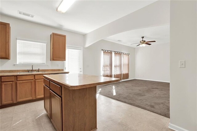 kitchen featuring a kitchen island, brown cabinets, light countertops, black appliances, and a sink