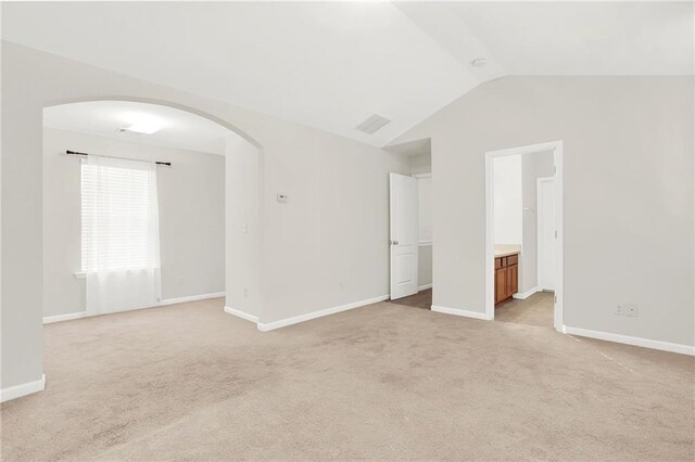 spare room featuring arched walkways, light carpet, lofted ceiling, and baseboards