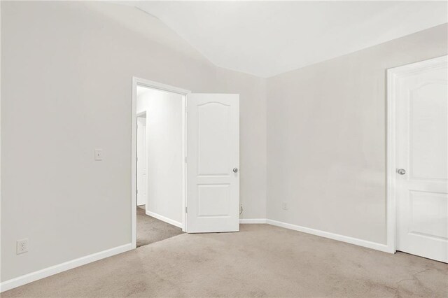 unfurnished room featuring baseboards, lofted ceiling, and light colored carpet