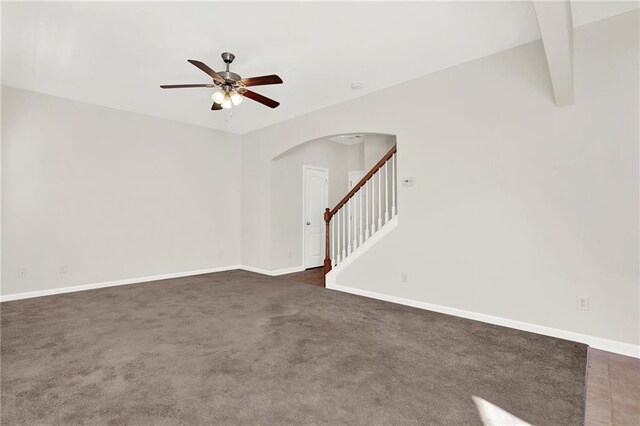 empty room featuring dark carpet, stairway, lofted ceiling with beams, a ceiling fan, and baseboards