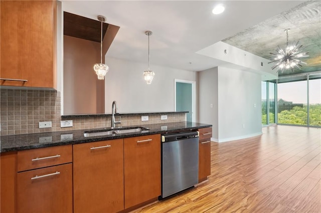 kitchen featuring sink, light hardwood / wood-style flooring, stainless steel dishwasher, dark stone counters, and pendant lighting