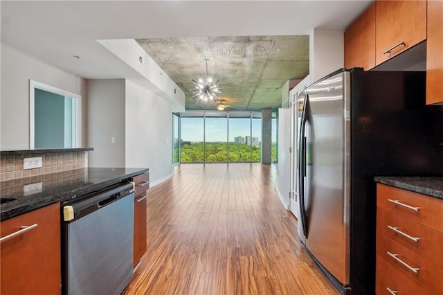 kitchen with floor to ceiling windows, light hardwood / wood-style flooring, dark stone countertops, appliances with stainless steel finishes, and a notable chandelier