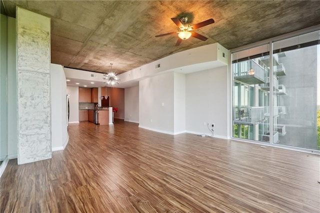 unfurnished living room featuring wood-type flooring, ceiling fan with notable chandelier, a wealth of natural light, and floor to ceiling windows