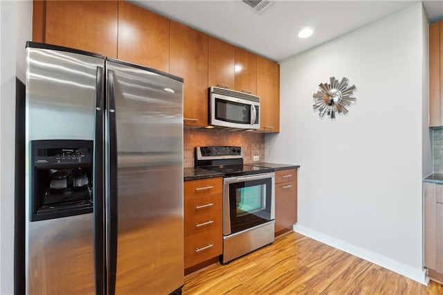 kitchen with decorative backsplash, stainless steel appliances, light hardwood / wood-style flooring, and dark stone countertops