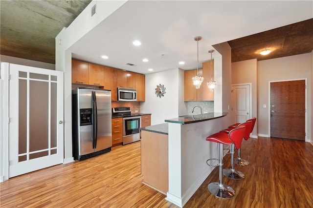 kitchen with stainless steel appliances, tasteful backsplash, kitchen peninsula, decorative light fixtures, and a kitchen bar