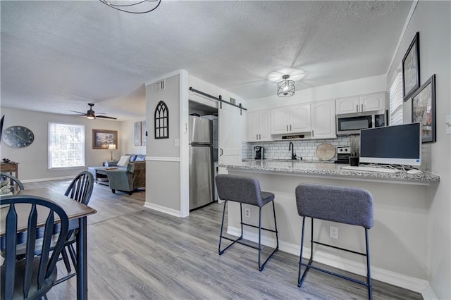 6700 Roswell Rd Unit 32C, Atlanta, GA 30328 - kitchen featuring stainless steel appliances, a textured ceiling, a barn door, a breakfast bar, and white cabinetry