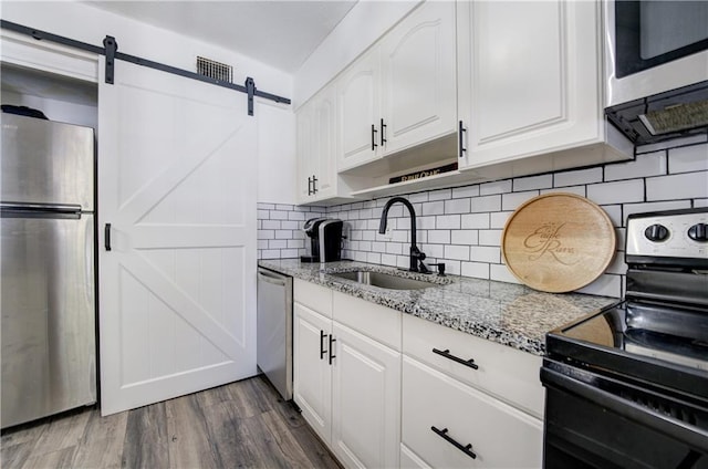 6700 Roswell Rd Unit 32C, Atlanta, GA 30328 - kitchen featuring appliances with stainless steel finishes, a sink, a barn door, light stone countertops, and white cabinets