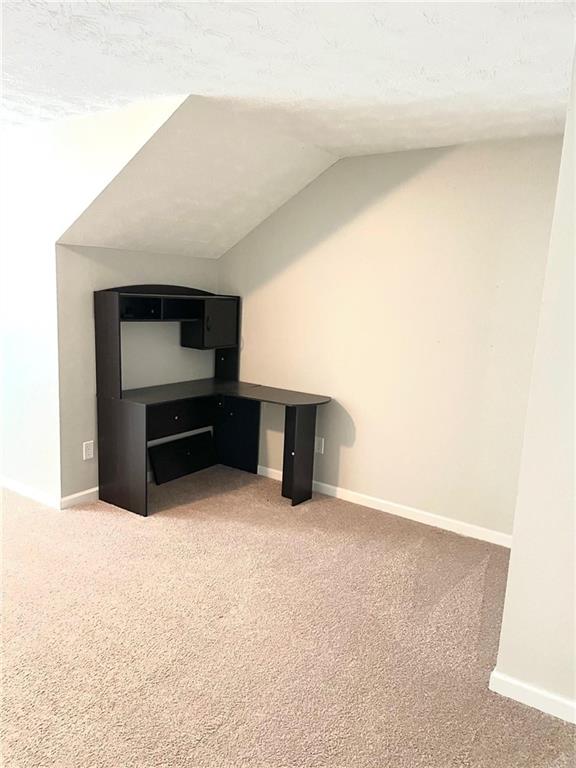 unfurnished living room with carpet flooring, a textured ceiling, and vaulted ceiling