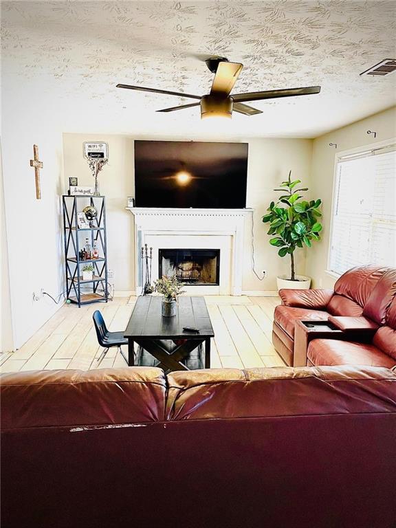 living room with ceiling fan, a textured ceiling, and light hardwood / wood-style flooring