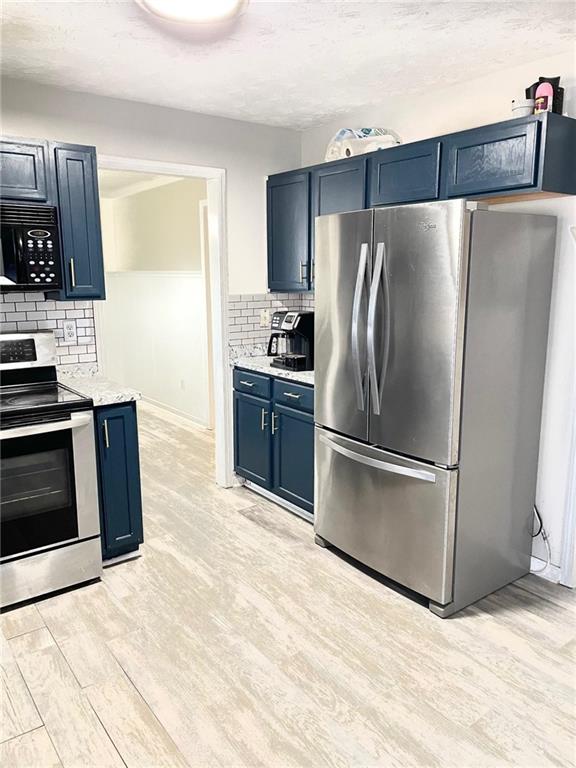 kitchen featuring tasteful backsplash, light wood-type flooring, a textured ceiling, blue cabinetry, and appliances with stainless steel finishes