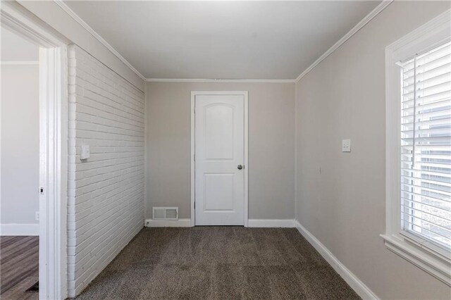 carpeted spare room featuring plenty of natural light, crown molding, and brick wall