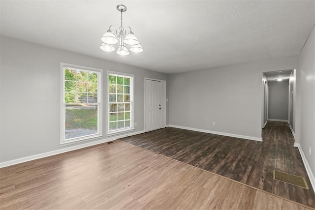 spare room with an inviting chandelier, a textured ceiling, and dark wood-type flooring