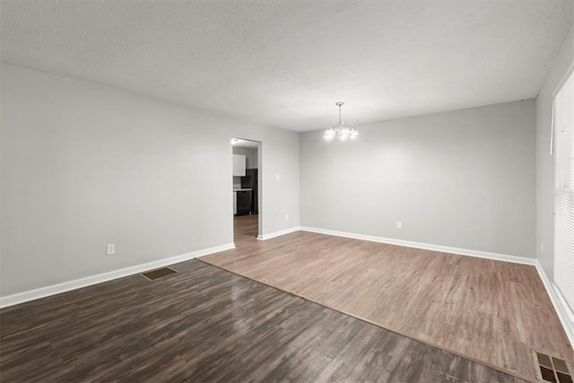 unfurnished room featuring a notable chandelier, a textured ceiling, and dark hardwood / wood-style flooring