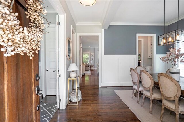 entryway featuring dark wood-type flooring, ornamental molding, wainscoting, and a decorative wall