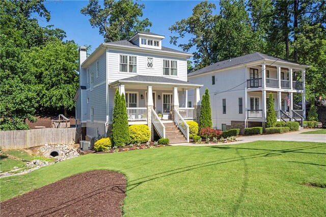american foursquare style home featuring fence, a front yard, a chimney, a porch, and stairway